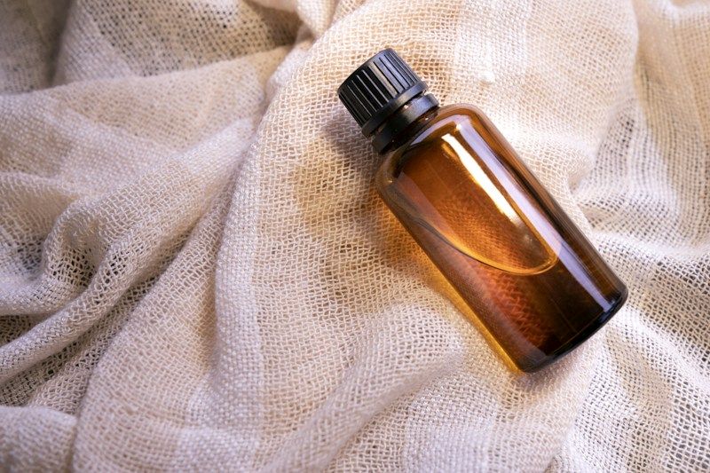 Flacon d'huile en verre ambré posé sur une étoffe claire