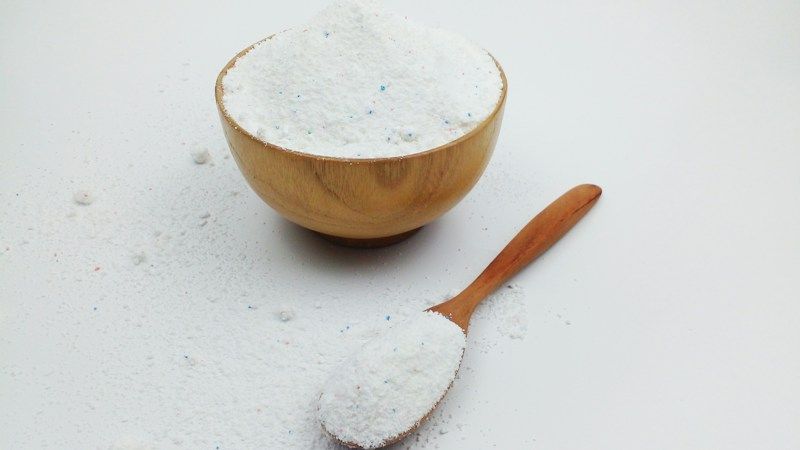 Bol en bois rempli de bicarbonate et cuillère sur fond blanc