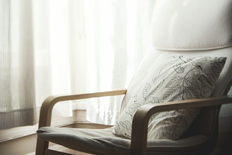 Fauteuil en bois et coussin clair près d'un voilage, dans une pièce lumineuse