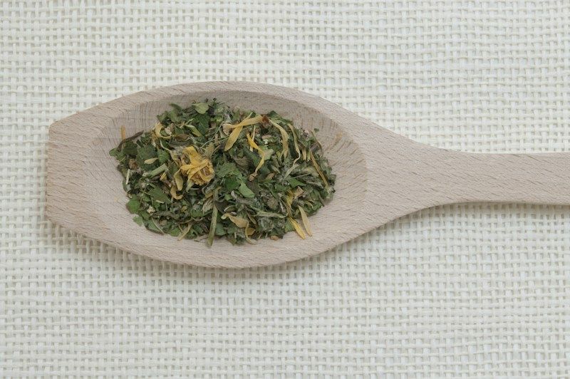 Cuillère en bois remplie de plantes séchées sur une toile de lin